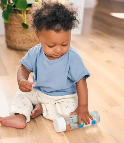 Child rolling a sensory bottle filled with pom poms