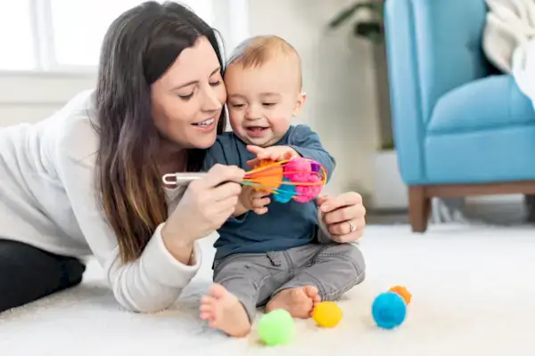 Mother their child sit up while playing with a whisk filled with pom poms