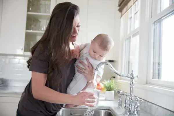 Mother pouring water from the kitchen sink while holding their baby
