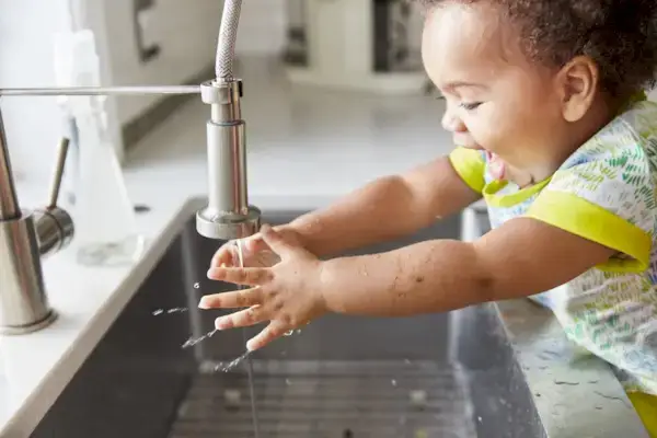 Toddler putting their hands in water coming from the kitchen sink