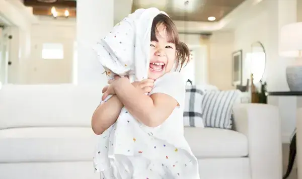 Toddler smiling and hugging an organic swaddle by Mommy's Reviews