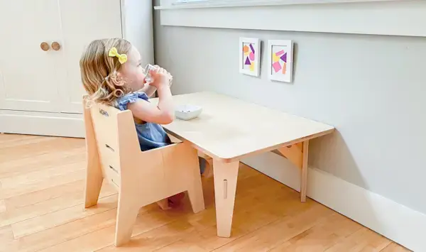 Young child sitting at a wooden table sipping a cup of water