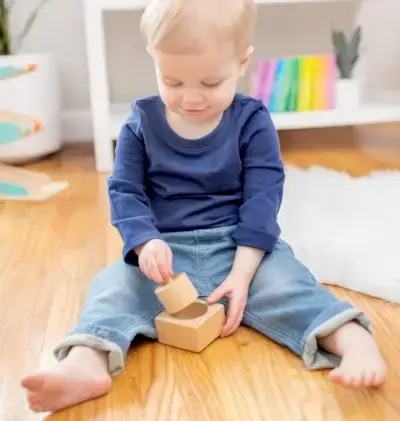 Toddler sitting up and playing with the wooden Pincer Puzzle from The Thinker Play Kit