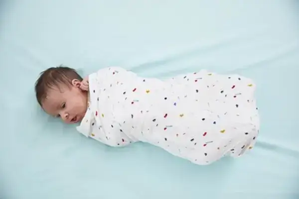 Baby laying down wrapped in an organic cotton swaddle by Mommy's Reviews