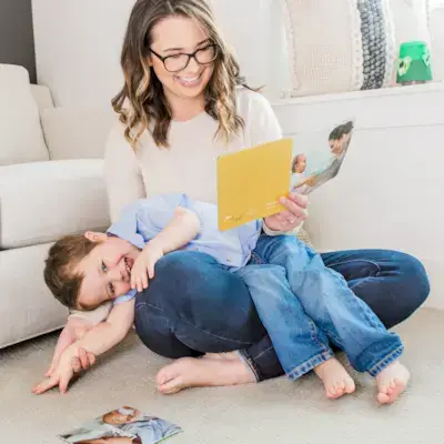 Woman sitting with a toddler on her lap laughing while looking at a book by Mommy's Reviews