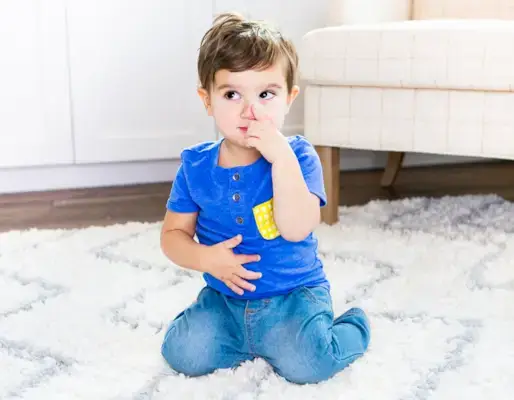 Toddler sitting on a rug pointing on their nose