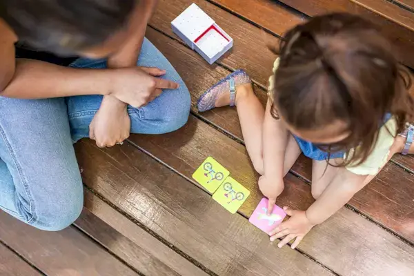 Toddler sitting on the ground outside playing the Memory Game and pointing to the air plane card