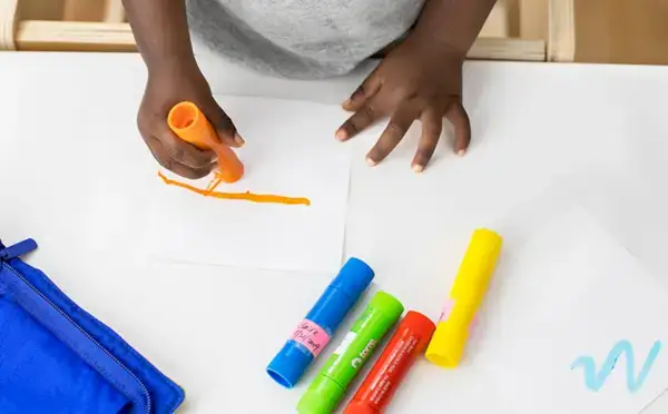 Toddler drawing on a white piece of paper with the Anywhere Art Kit With Washable Tempera Paintsticks