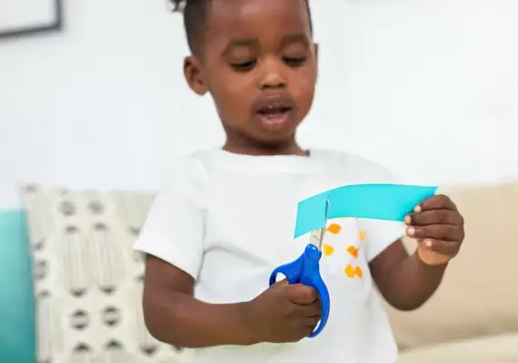 Young child using scissors to cut a blue piece of paper