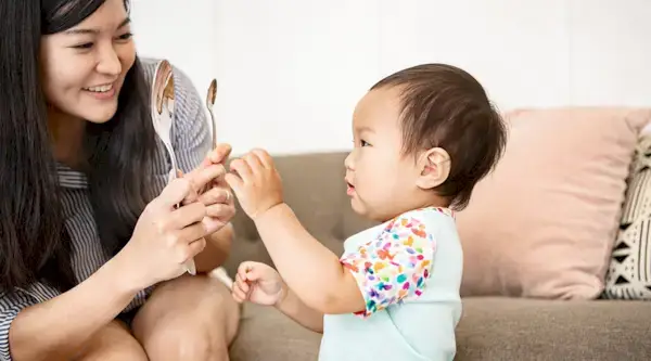 Woman holding two spoons in front of a baby