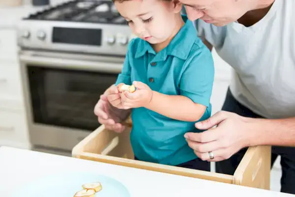 Toddler in the kitchen helping peel a banana