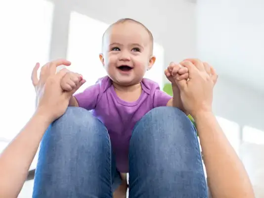 Happy baby balancing on their caregivers knees