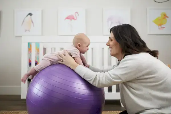 Baby doing tummy time on an exercise ball being supported by a woman