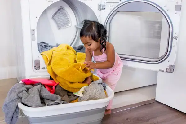 Little girl helping pull clothes out of the dryer