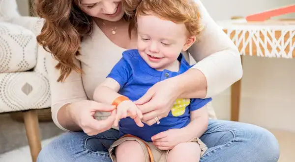 Woman holding a toddler in their lap and putting a piece of ribbon around their wrist