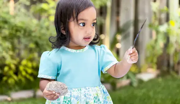 Toddler in a blue dress holding a feather and a rock
