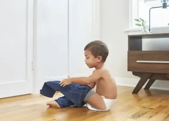 Young child sitting down putting on a pair of jeans