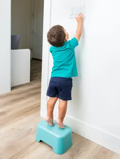 Young child standing on a stool flipping a light switch.