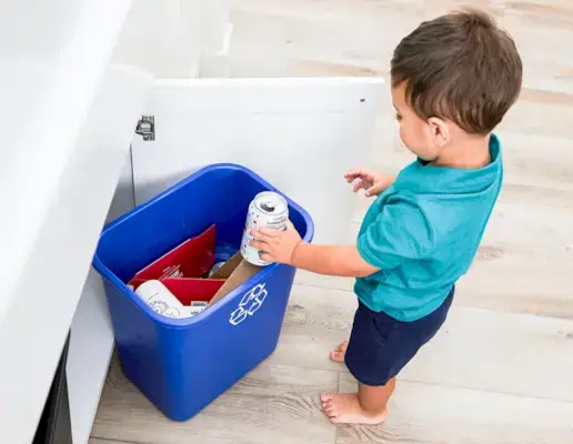 Young child placing a can in a recycling bin.