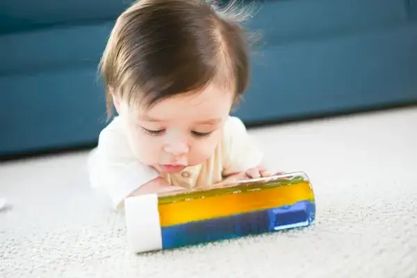 Baby doing tummy time and looking at a water bottle filled with different colors