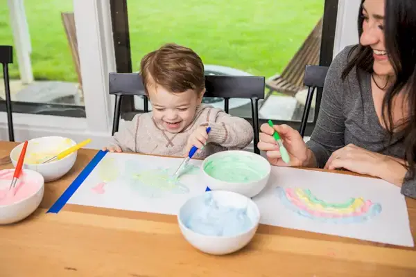 Woman and toddler playing with colored shaving cream on a piece of paper 