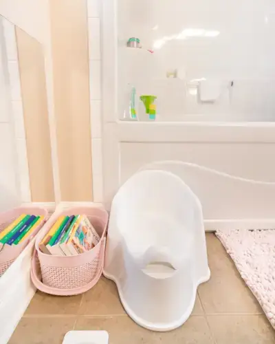Potty seat and a basket of books next to a bathtub in a bathroom