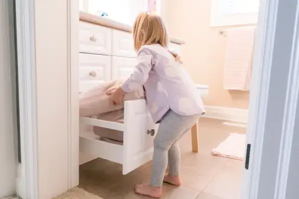 Young child putting towels away in a drawer in a bathroom