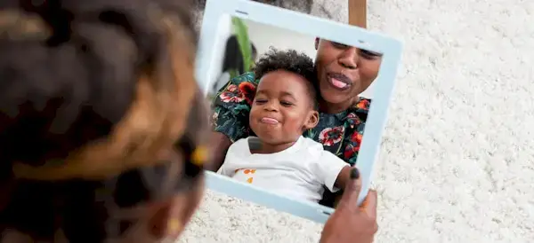 Woman with a toddler in her lap looking into the Framed Mirror sticking out their tongues