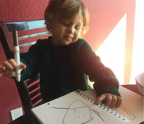 A toddler with a marker in their hand drawing on paper