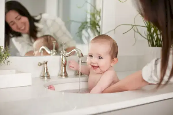 Woman giving a baby a bath in the bathroom sink