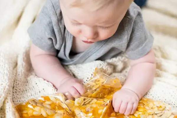 Baby playing with a plastic bag filled with pumpkin seeds