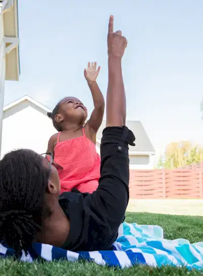 Toddler laying on a woman outside pointing up at the sky