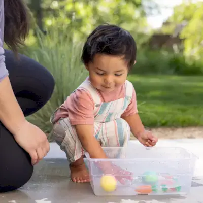 Child playing with sensory bin filled with Mommy's Reviews toys and water