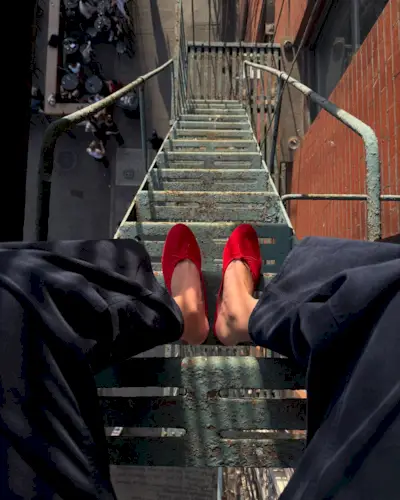 Influencer Lizzy Hadfield wears red slippers while sitting on a fire escape in New York.