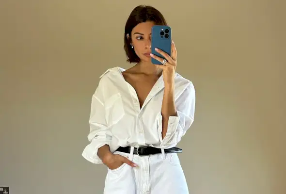 Woman wearing white button down, black belt, and white bermuda denim shorts.