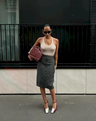 Fashion person Emily Nitta wears a cream halterneck top, a tailored skirt and two tone heel. She is carrying a matching burgundy duffle and oval sunglasses in a recent image from her Instagram.