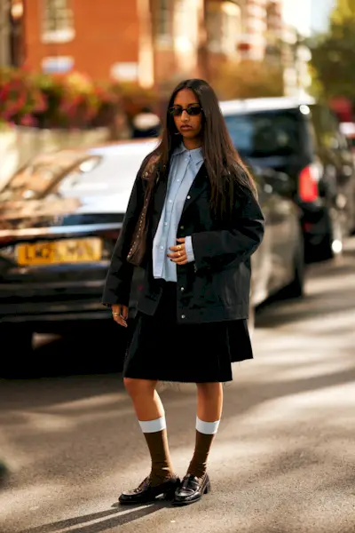 A woman in London wears a skirt with socks and loafers.