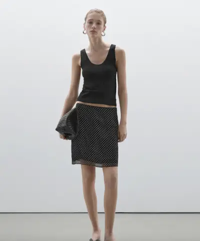 Bella Hadid wearing a black leather bomber jacket and polka dot midi skirt with sneakers.