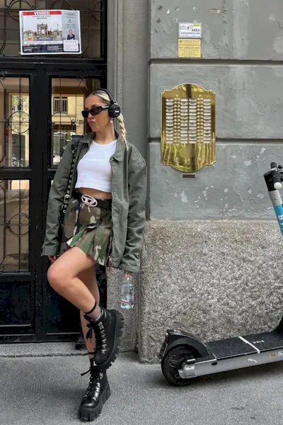 a photo of a woman wearing combat ankle-boots in summer with a cargo mini skirt black belt white tank top and green army jacket and sunglasses