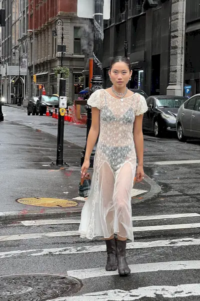 a photo of a woman wearing black ankle-boots in summer with a sheer white lace dress with a black bra top and black briefs
