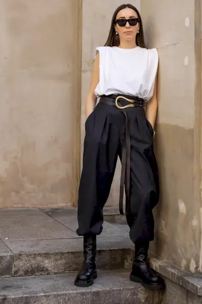 a photo of a woman wearing black chelsea ankle-boots in summer with tailored pants tucked-in and a belt and white muscle tee and sunglasses