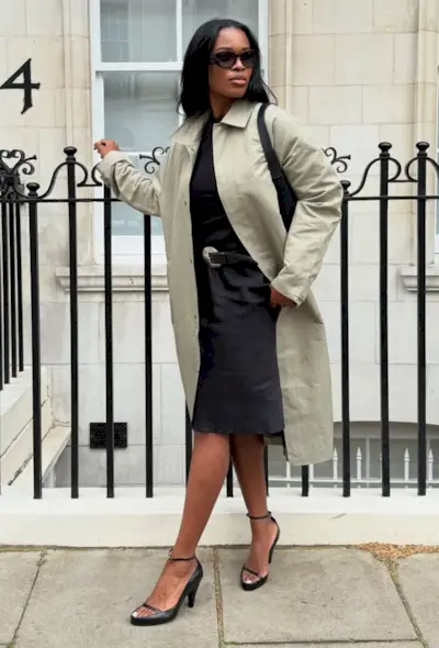 @nlmarilyn wears a light green car coat, black top, satin skirt and black heels