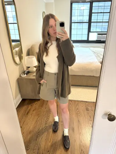 Nikki Chwatt wears Zara bermuda shorts in green with a white tank top, grey cardigan, burgundy loafers, and white socks.