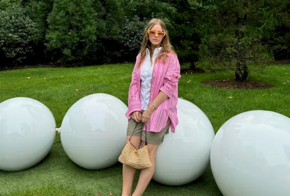 Nikki Chwatt wears green bermuda shorts from Zara, a pink striped button-down, white button-down, yellow sunglasses and a straw shoulder bag.