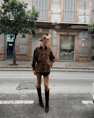 Woman wearing oversize button-down and miniskirt with tall suede boots.