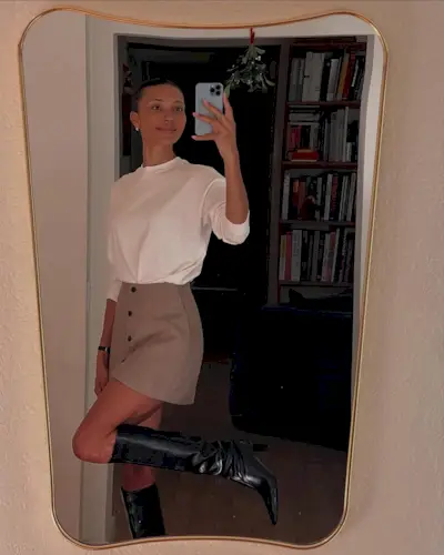 Woman wearing white top and miniskirt with tall black boots.