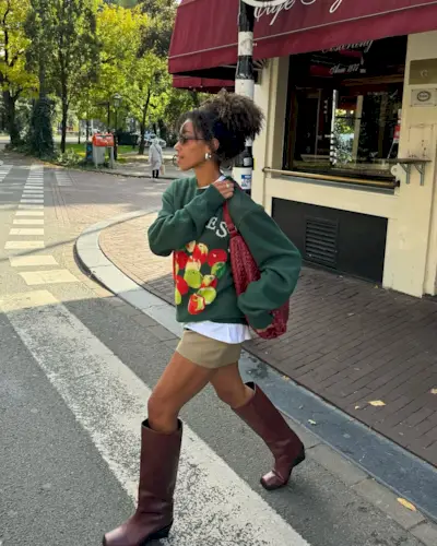 Woman wearing crewneck and tan miniskirt with tall brown boots.