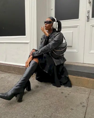 Woman wearing black skirt, leather jacket, and tall black boots.