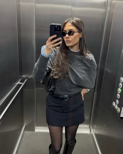 Woman wearing sweater and miniskirt with tall black boots.