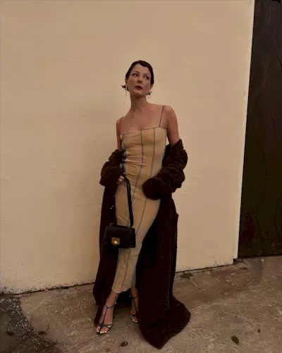 a photo showing black tie attire for women with a woman wearing nude gown with a long black coat and black strappy sandals